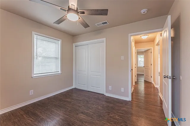 an empty room with wooden floor fan and windows