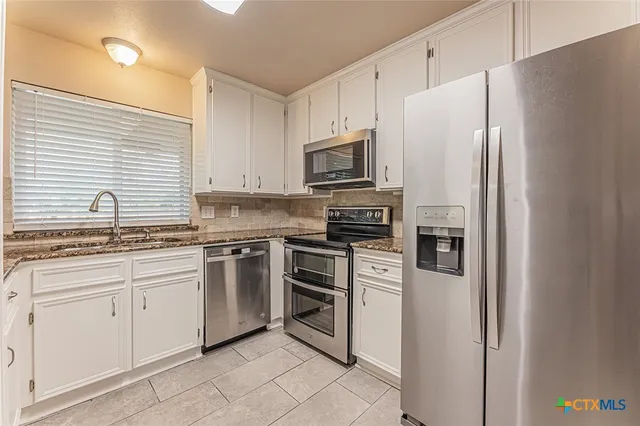 a kitchen with stainless steel appliances granite countertop a refrigerator a stove a sink and white cabinets