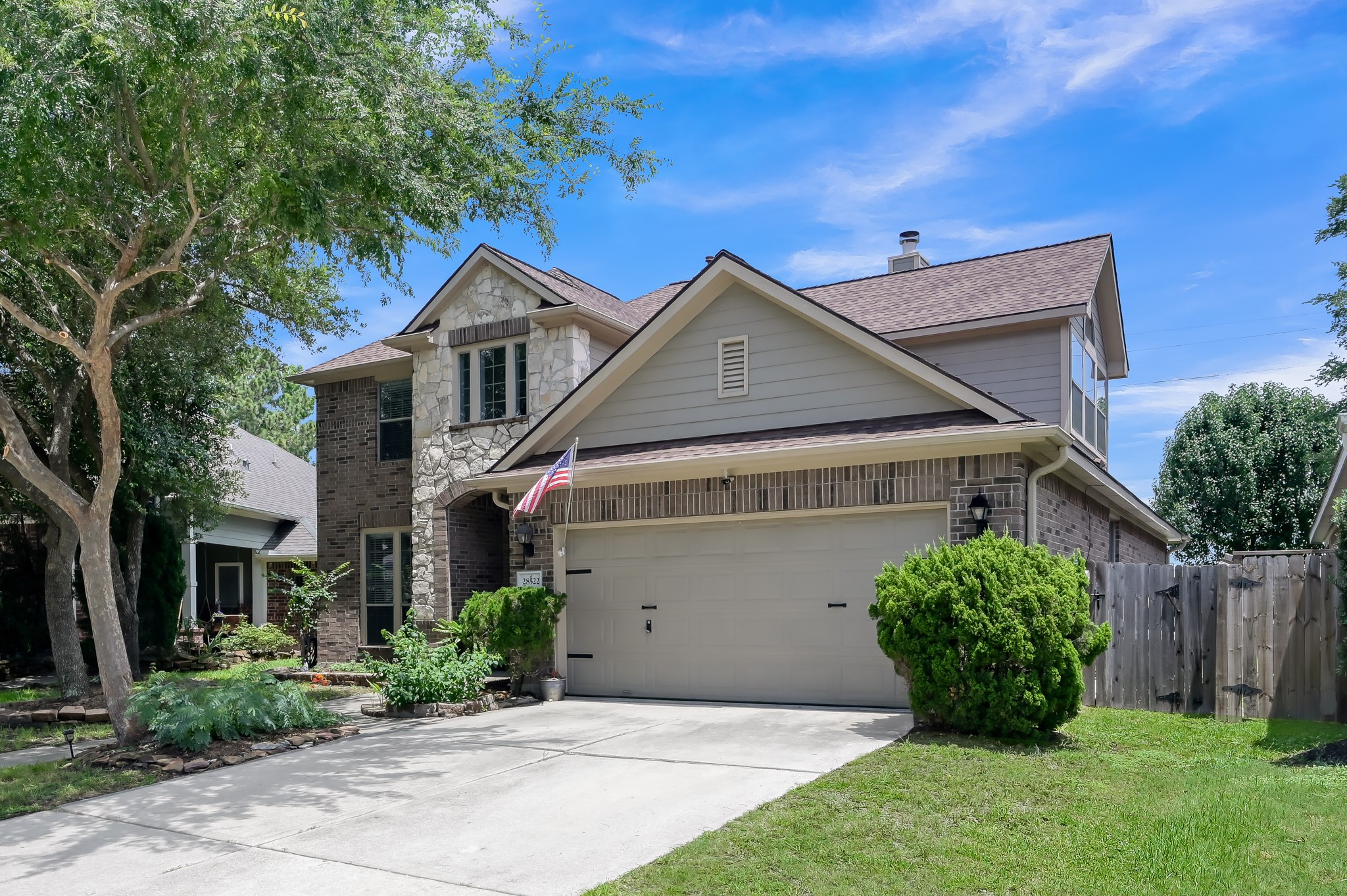 Gorgeous daytime exterior featuring mature trees, lush landscaping, and a timeless brick-and-stone façade. Spacious driveway and covered front entry add both convenience and charm.