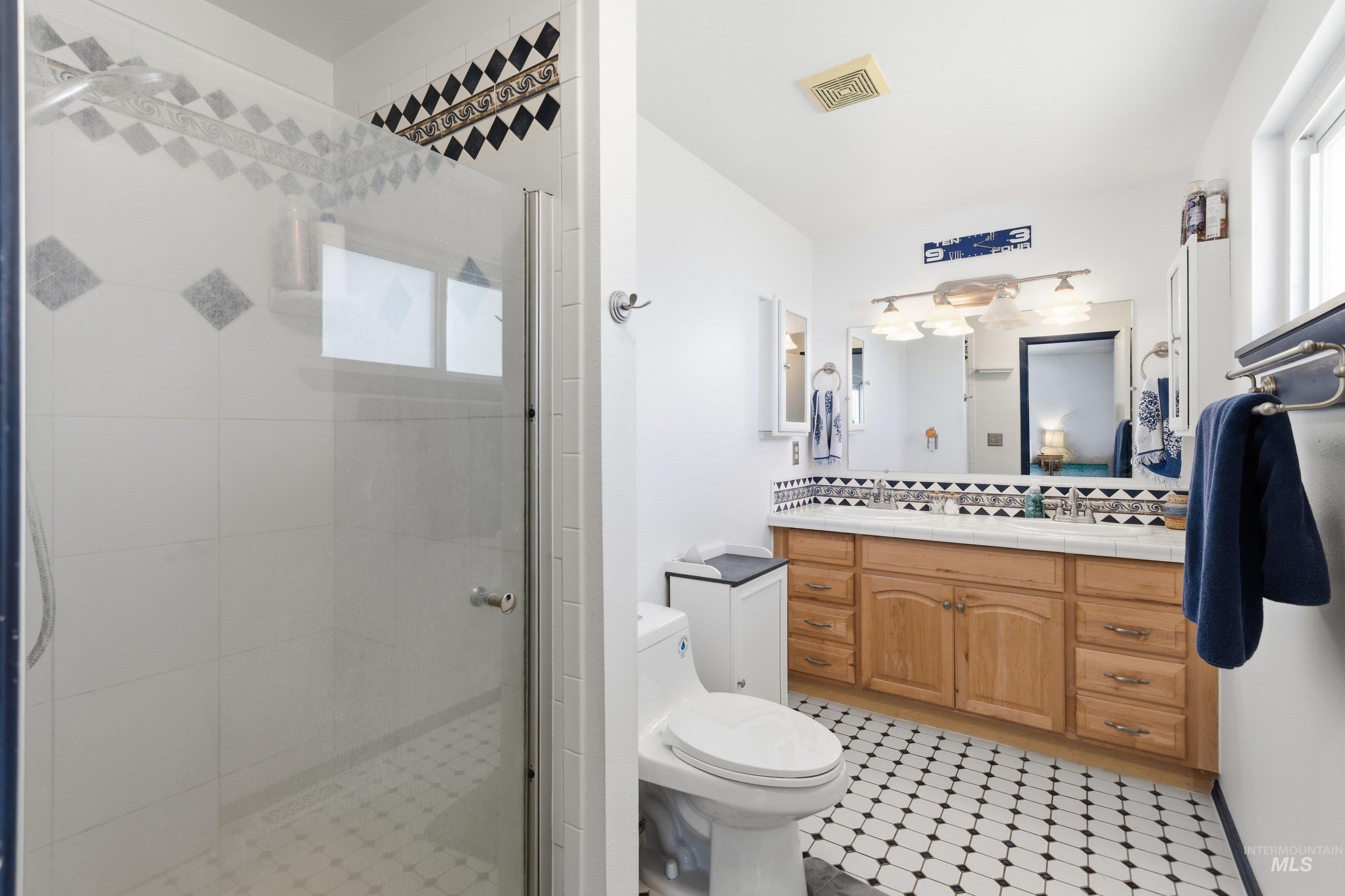 15095 David Street Caldwell, ID 83607 - Photo 22 of 39 Bathroom featuring a glass-enclosed shower, dual vanity with wood cabinetry, and black and white patterned floor tiles