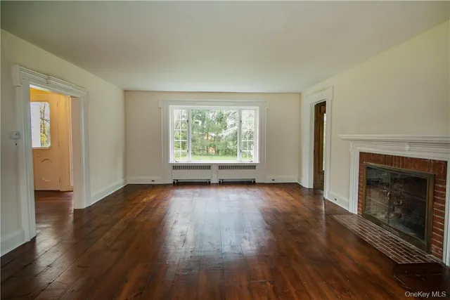 an empty room with wooden floor fireplace and windows