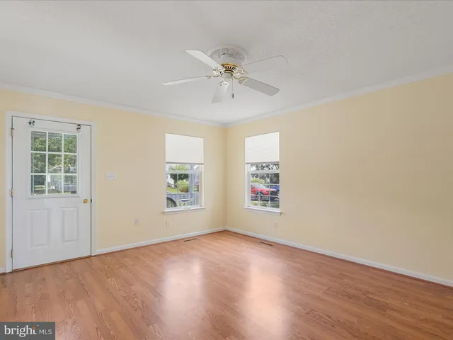 an empty room with wooden floor chandelier fan and windows