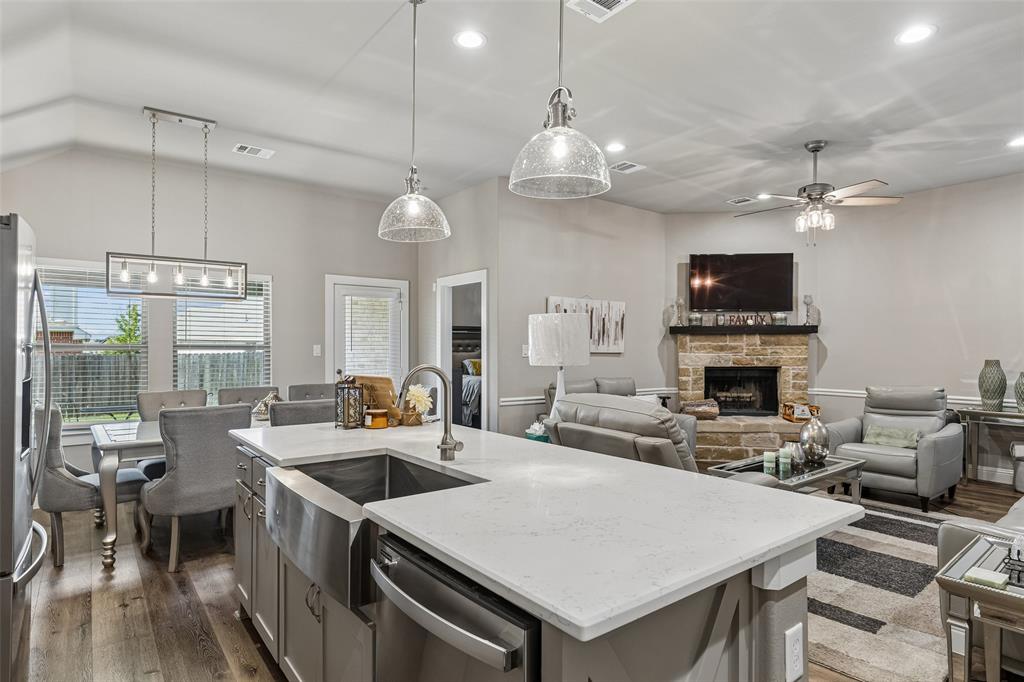 108 Maverick Lane Pilot Point, TX 76258 - Photo 8 of 27 Open-concept kitchen featuring a large island with a farmhouse sink, stainless steel appliances, wood-finish flooring, recessed lighting, and a stone fireplace
