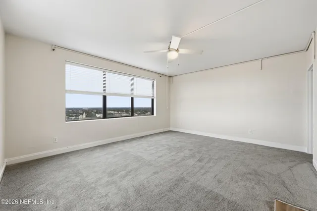 an empty room with chandelier fan and windows