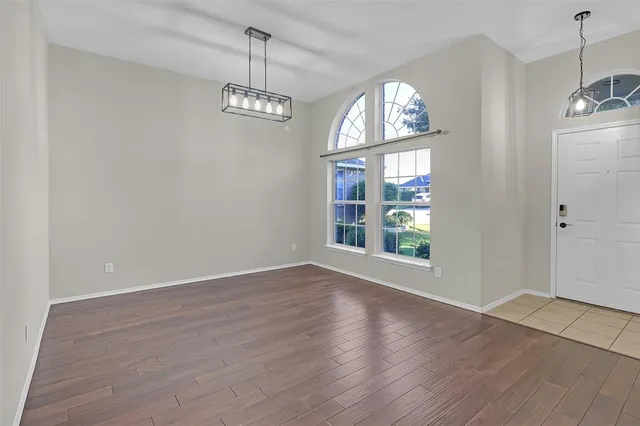 an empty room with wooden floor chandelier and windows