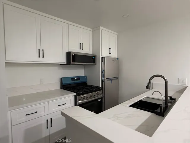 a kitchen with stainless steel appliances kitchen island a refrigerator a sink a stove and white cabinets