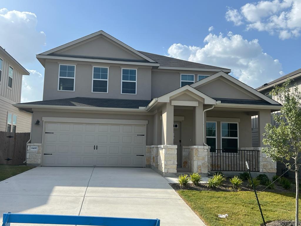 Two-story home featuring a stucco exterior with stone accents, an attached two-car garage, a covered front porch with iron railing, and a concrete driveway