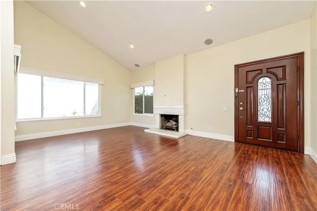 an empty room with wooden floor fireplace and windows
