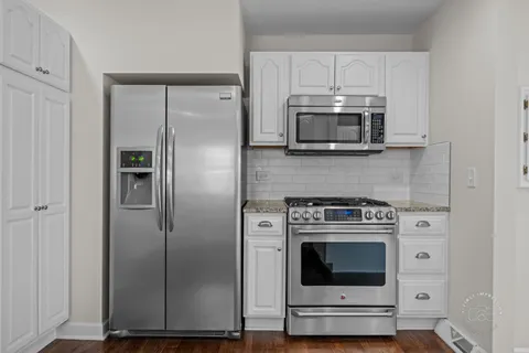 a kitchen with stainless steel appliances granite countertop a refrigerator a sink dishwasher a stove and white cabinets with wooden floor