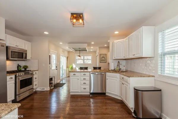 a kitchen with stainless steel appliances granite countertop a stove top oven a sink dishwasher and a refrigerator with wooden floor