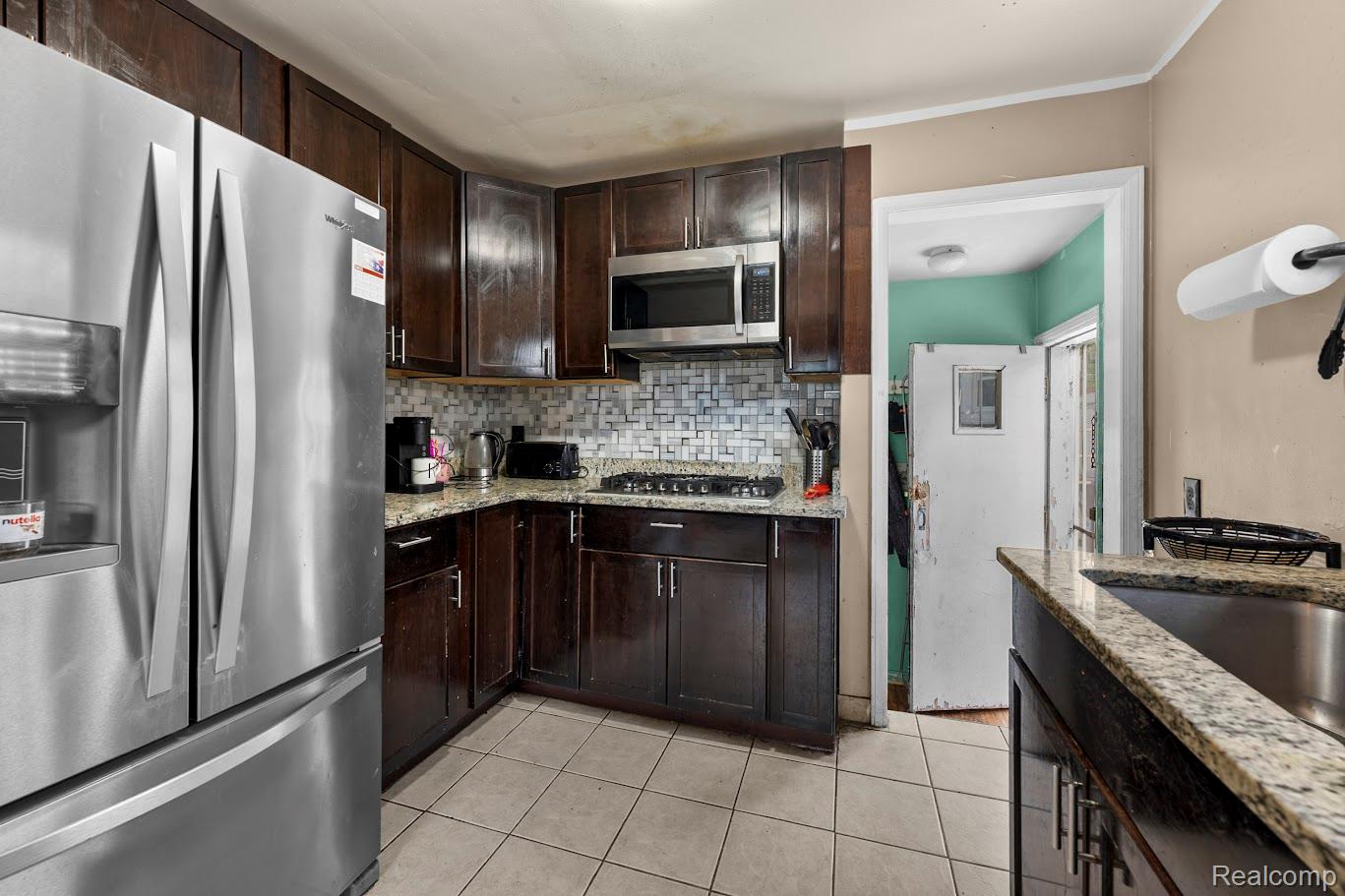 6800 Longacre Street Detroit, MI 48228 - Photo 11 of 24 Kitchen with stainless steel appliances, dark wood finish cabinets, light stone countertops, light tile patterned floors, and backsplash