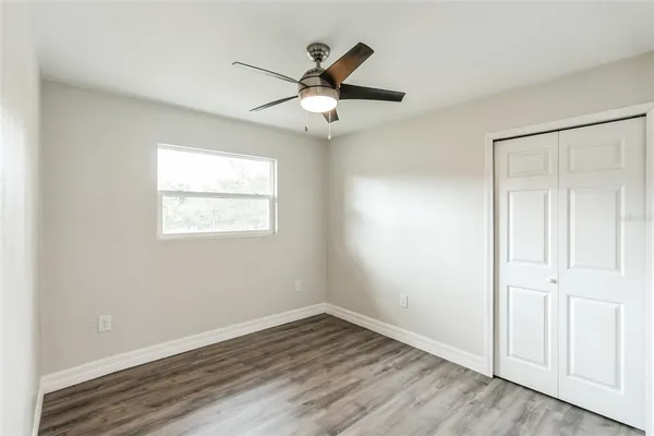an empty room with wooden floor ceiling fan and windows