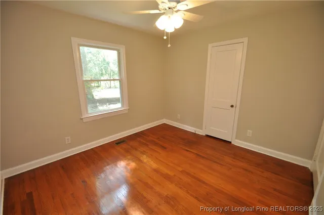 an empty room with wooden floor fan and windows