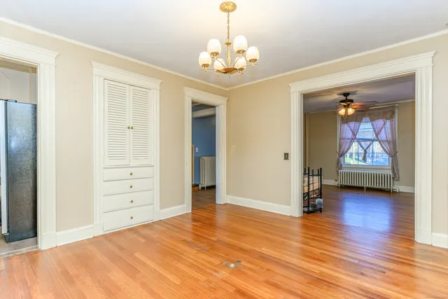 an empty room with wooden floor chandelier and windows