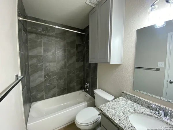 a bathroom with a granite countertop bathtub shower sink vanity and toilet