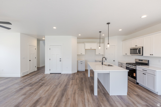 195 West Harmony Rdg Parkway, Unit 601 Mapleton, UT 84664 - Photo 11 of 23 Open-concept kitchen and living area featuring wood-finish flooring, white cabinetry, a kitchen island with sink, stainless steel appliances, and recessed lighting