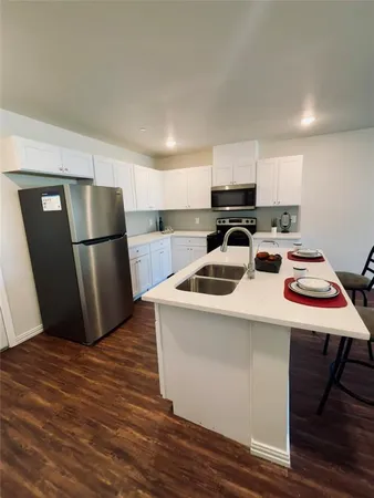 a kitchen with stainless steel appliances kitchen island granite countertop a sink a stove a dining table and chairs with wooden floor