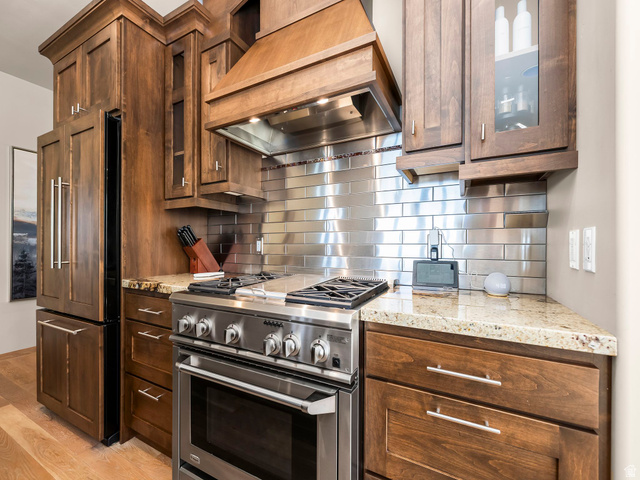 22677 East Snowbird Drive, Unit 47 Helper, UT 84526 - Photo 12 of 43 Kitchen with glass fronted cabinets, high quality appliances, light stone counters, light wood-style flooring, and decorative backsplash