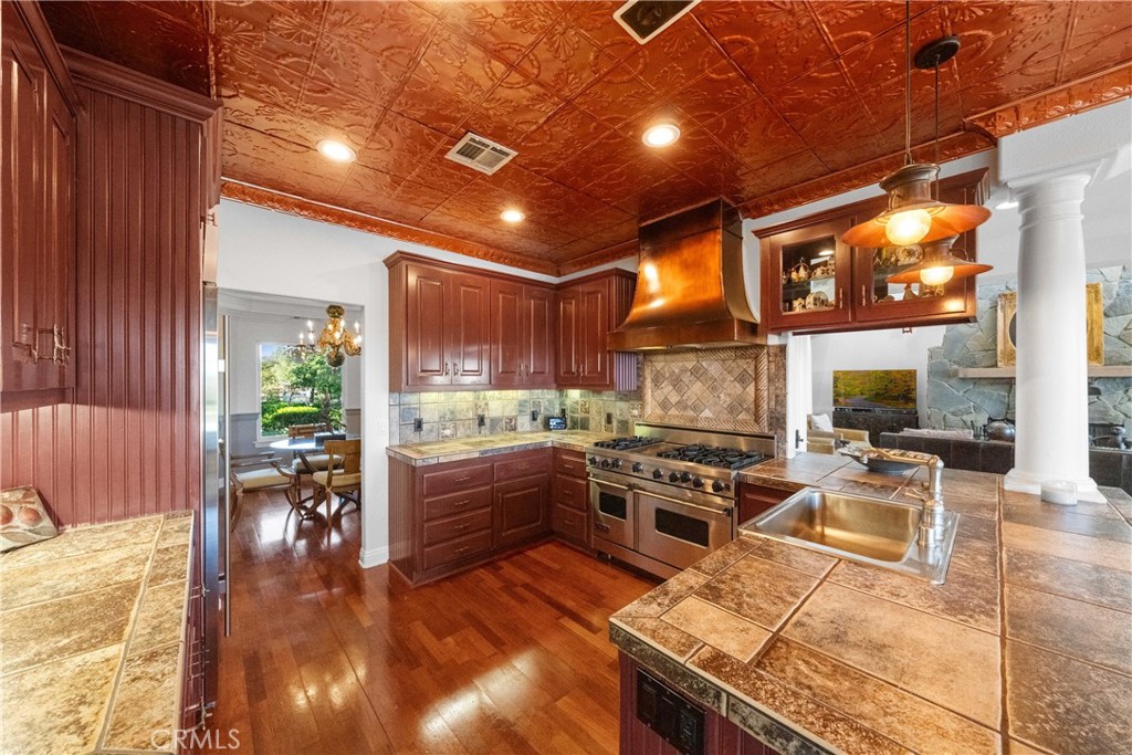 39817 Calle Cabernet Temecula, CA 92591 - Photo 52 of 75 a kitchen with stainless steel appliances granite countertop a stove top oven a dining table and chairs with wooden floor