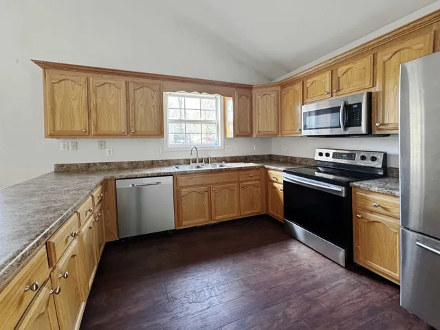 a kitchen with stainless steel appliances granite countertop a sink a stove top oven a refrigerator with grey cabinets and wooden floor