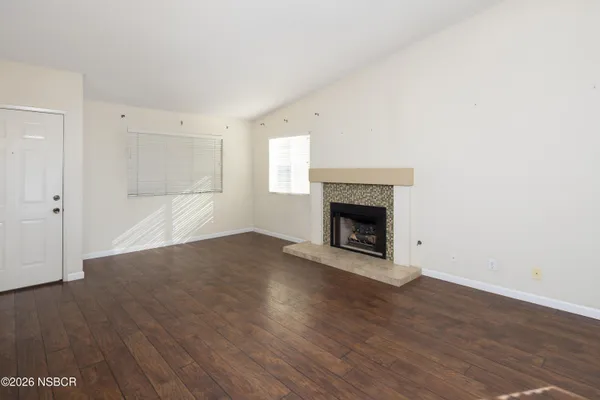 a view of an empty room with wooden floor fireplace and a window