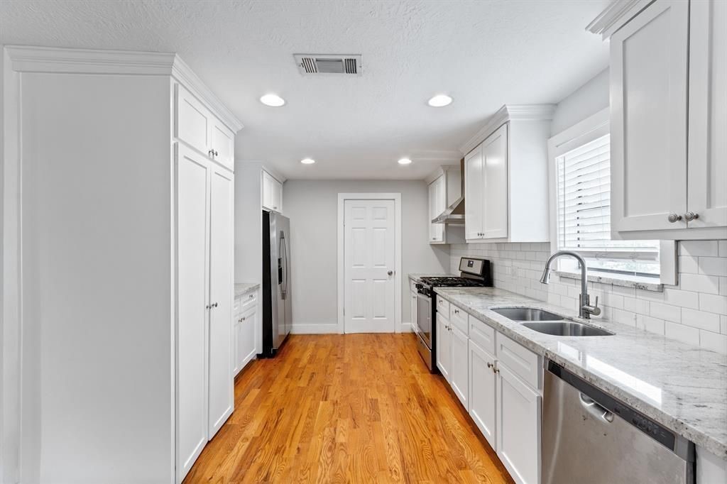 1305 Idylwild Street Houston, TX 77009 - Photo 10 of 31 This kitchen features sleek white cabinetry, stainless steel appliances, and granite countertops. The hardwood floors add warmth, while ample natural light enhances the spacious feel. Perfect for modern cooking and entertaining.
