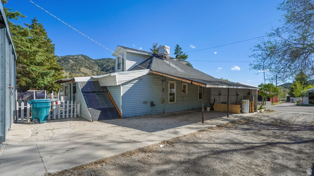44 Shriver Street Eureka, UT 84628 - Photo 28 of 43 Light blue siding exterior with a shingled roof, featuring an attached carport and a white picket fence enclosing a small side yard
