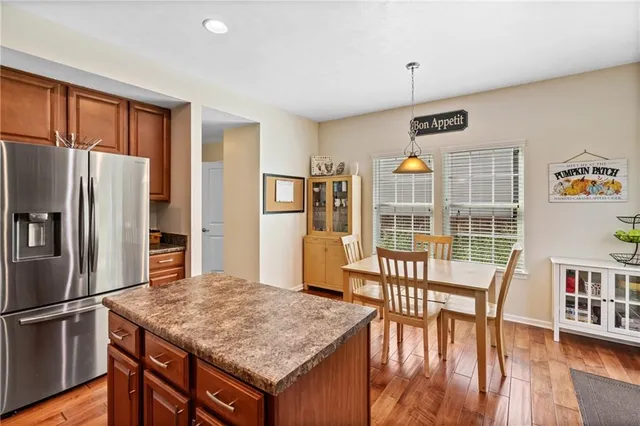 a kitchen with stainless steel appliances granite countertop a refrigerator a stove top oven a dining table and chairs with wooden floor