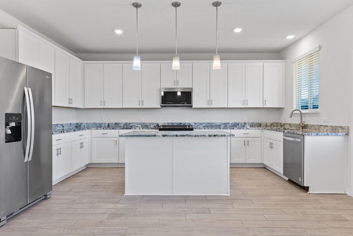905 Duskywing Way Georgetown, TX 78626 - Photo 5 of 21 a white kitchen with granite countertop a stove a sink a refrigerator and white cabinets with wooden floor