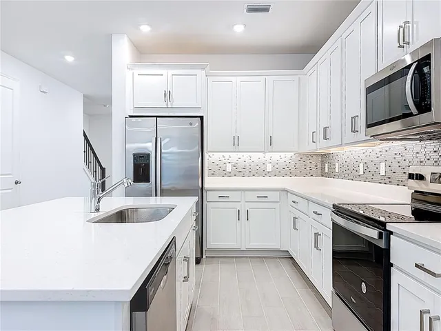 a kitchen that has a refrigerator a stove and white cabinets with wooden floor