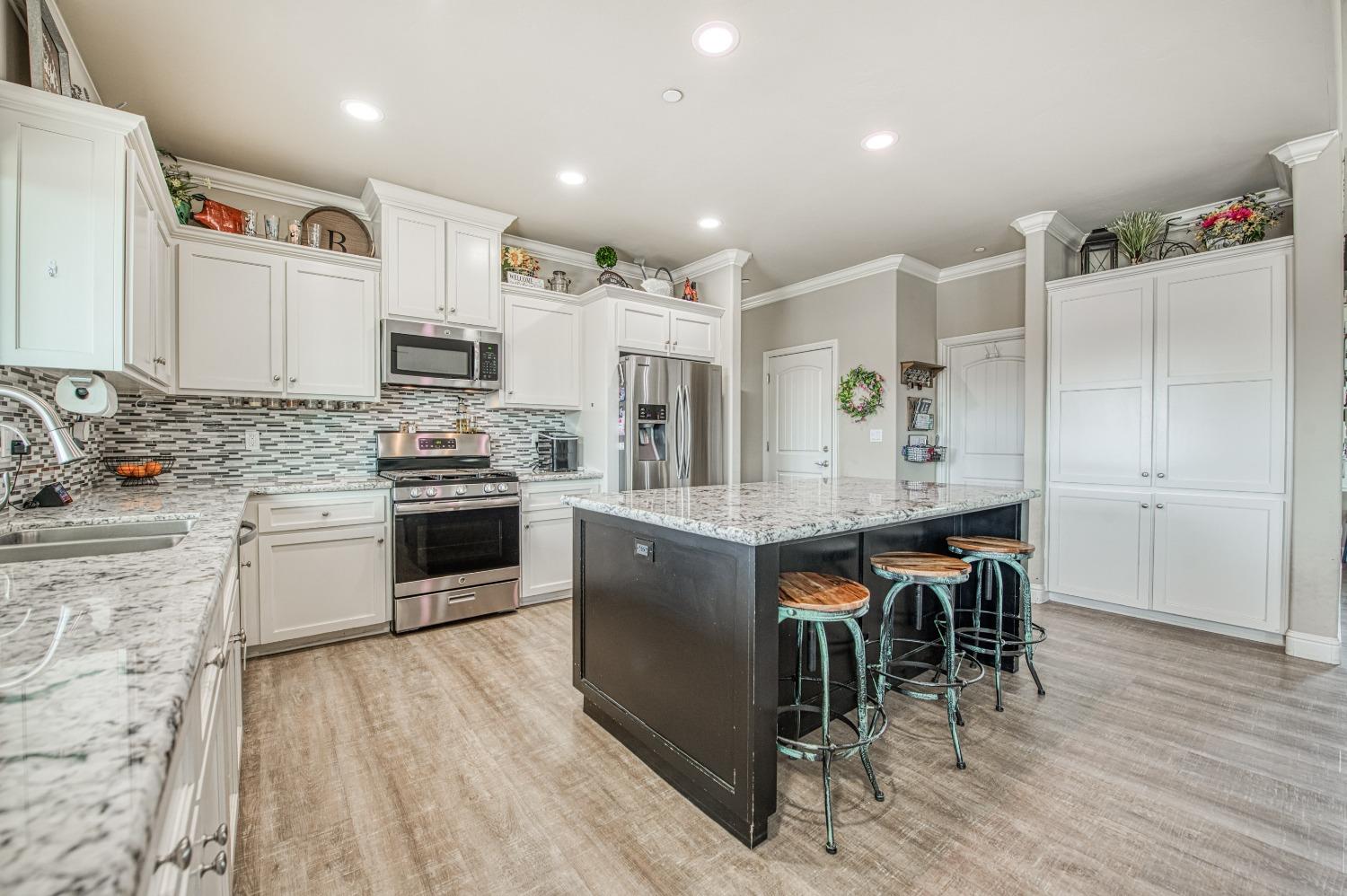 36919 Ave 17 1/2 Madera, CA 93636 - Photo 15 of 77 a open kitchen with stainless steel appliances granite countertop a stove top oven a sink dishwasher and white cabinets with wooden floor