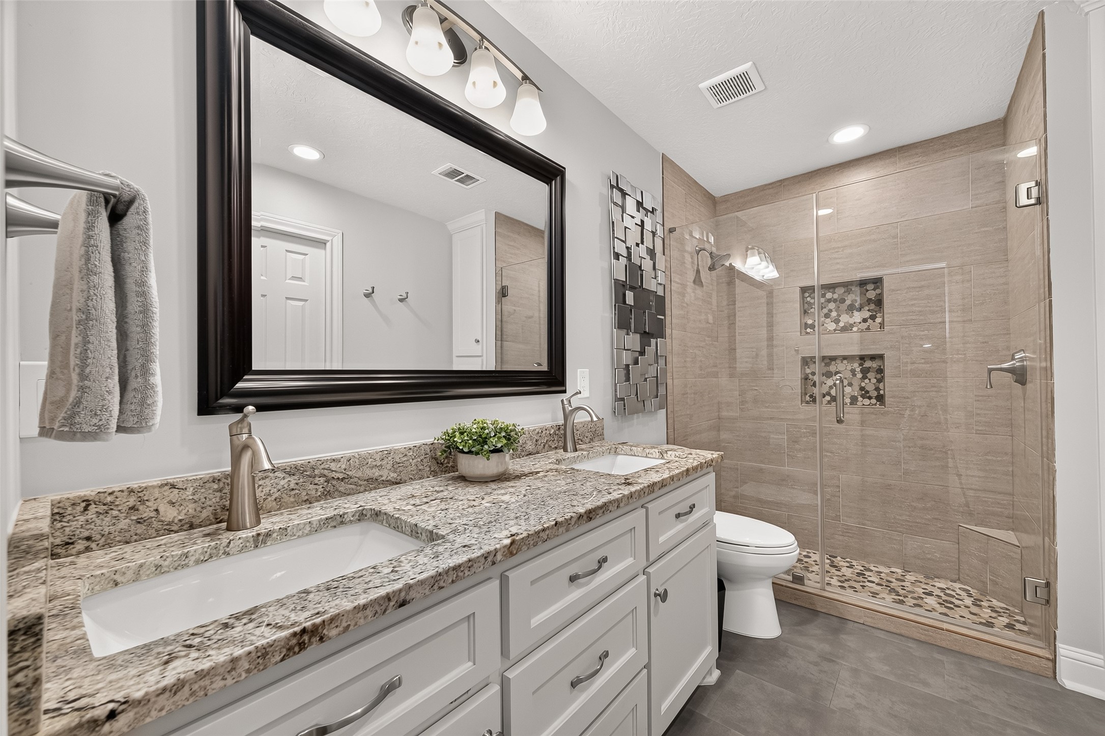 24719 Wilderness Road Spring, TX 77380 - Photo 30 of 42 This bathroom features a sleek double vanity with granite countertops, a large mirror, and modern fixtures. The spacious walk-in shower showcases stylish tile work and built-in shelving.