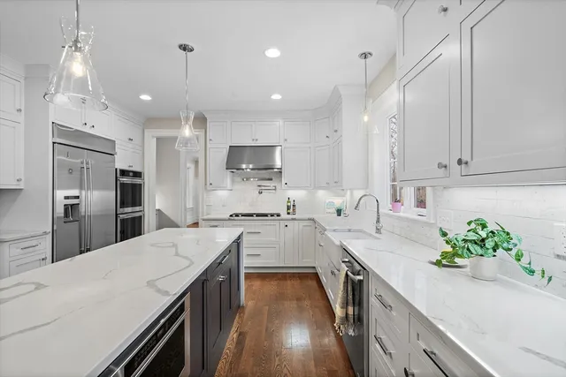 a kitchen with stainless steel appliances kitchen island granite countertop a sink a stove a refrigerator cabinets and wooden floor