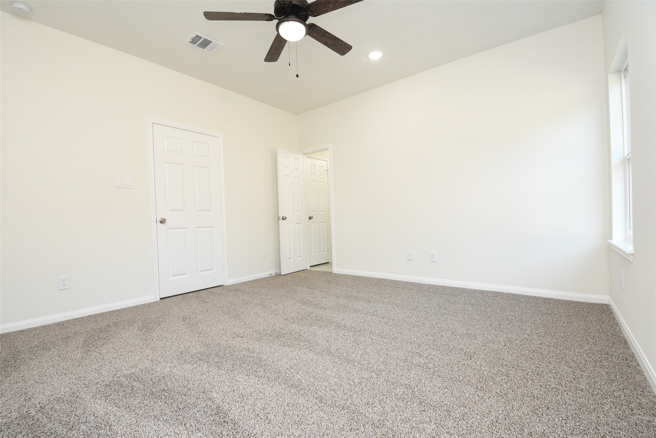 2811 Topiary Lane Houston, TX 77014 - Photo 23 of 32 A clean, empty room with beige carpet, white walls, multiple doors, and a ceiling fan. Brightly lit with natural light from a window.