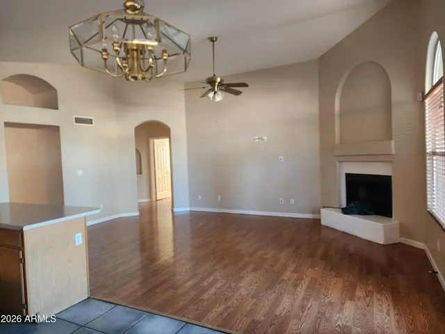 an empty room with wooden floor a chandelier fan a fireplace and windows
