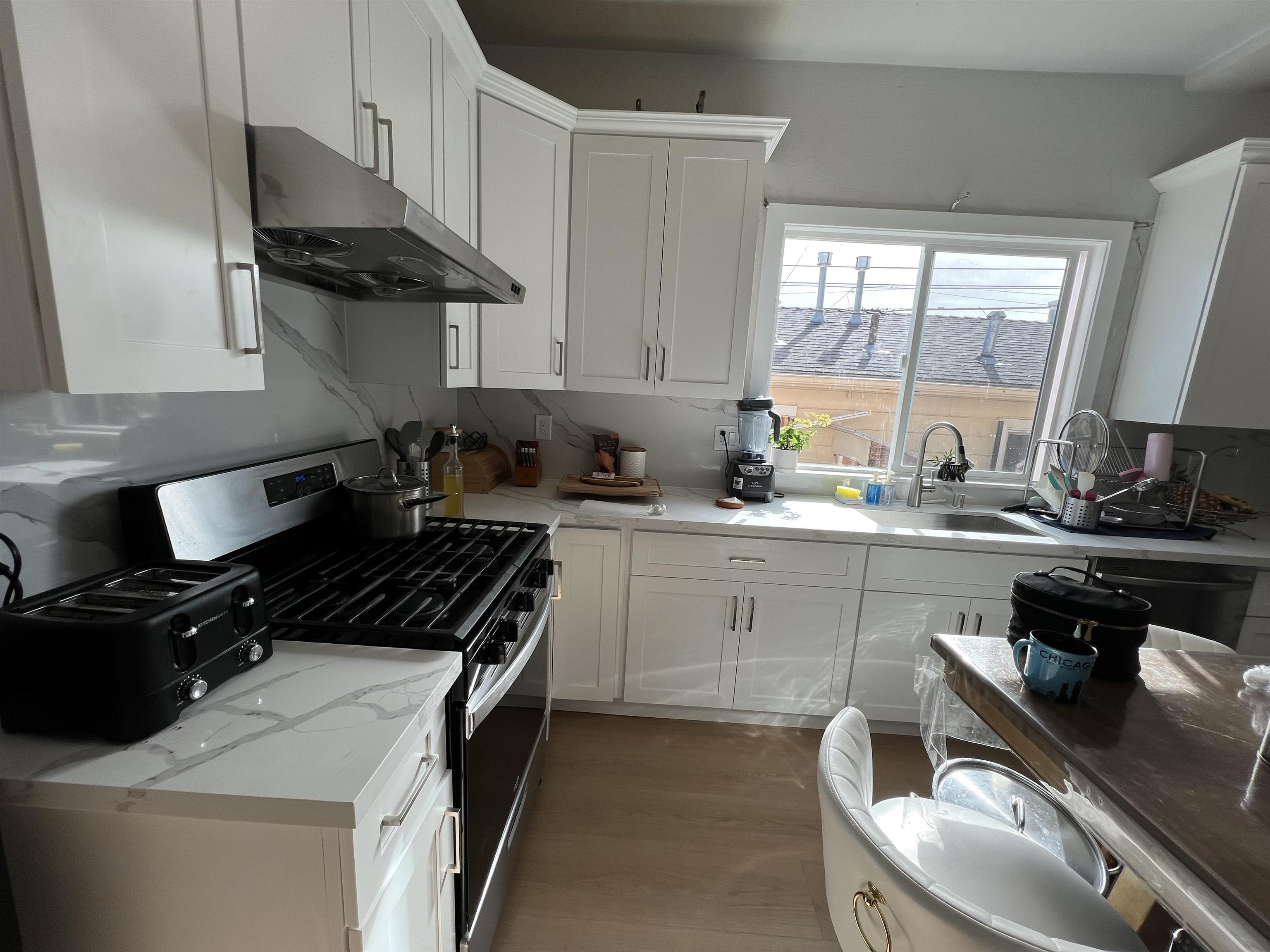 1803 Rosedale Avenue Oakland, CA 94601 - Photo 27 of 28 Kitchen with stainless steel gas range, white cabinetry, under cabinet range hood, and light stone counters