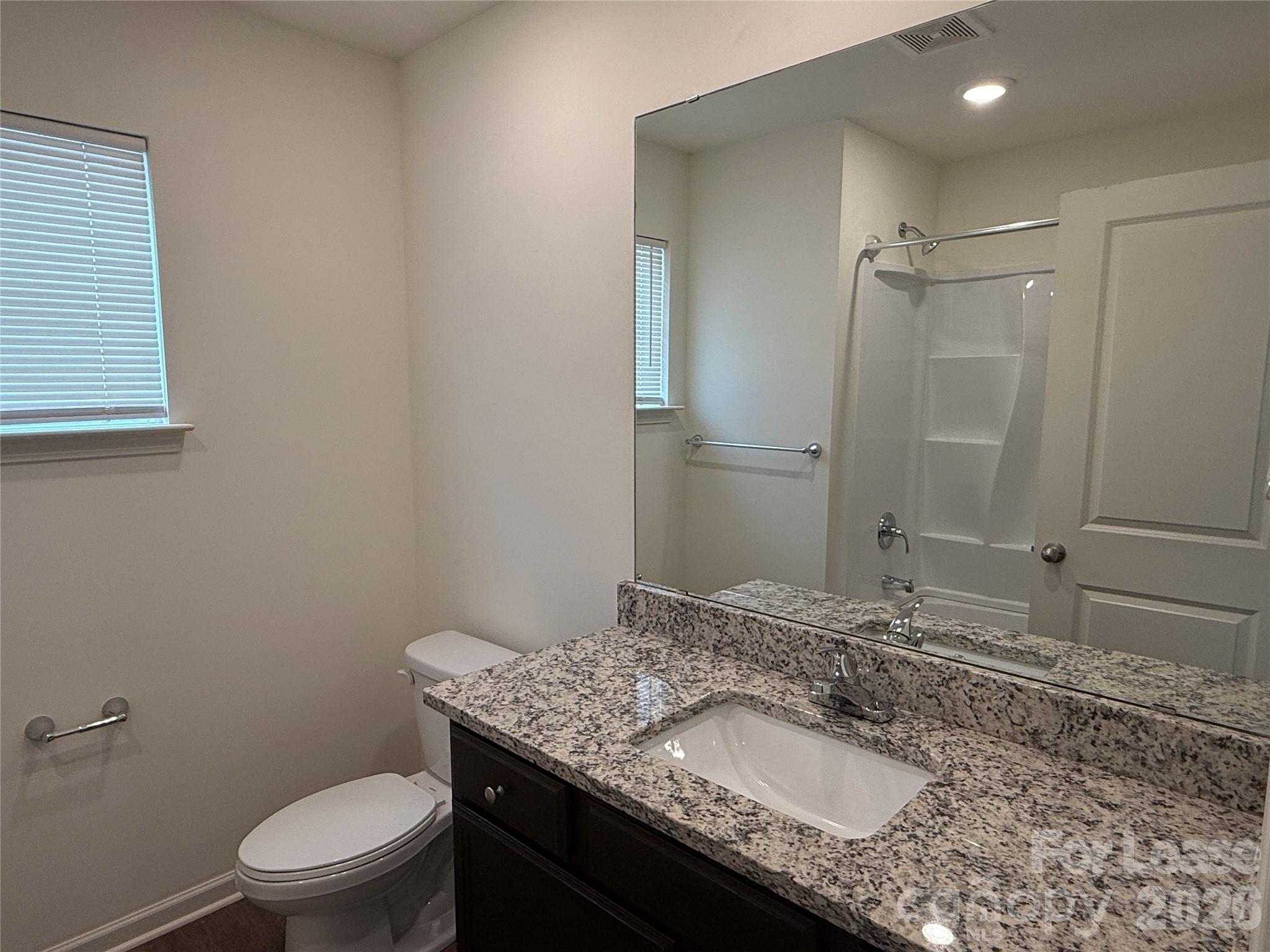 2021 Oakdale Road, Unit K Charlotte, NC 28216 - Photo 10 of 13 a bathroom with a granite countertop sink a toilet a mirror and shower