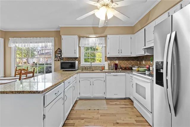 a kitchen with stainless steel appliances granite countertop a refrigerator a sink a stove and white cabinets
