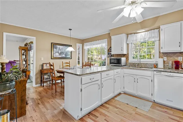 a open kitchen with granite countertop a stove a sink dishwasher and white cabinets with wooden floor