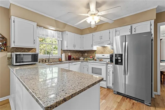 a kitchen with stainless steel appliances granite countertop a refrigerator a stove a sink a island with white cabinets and wooden floor