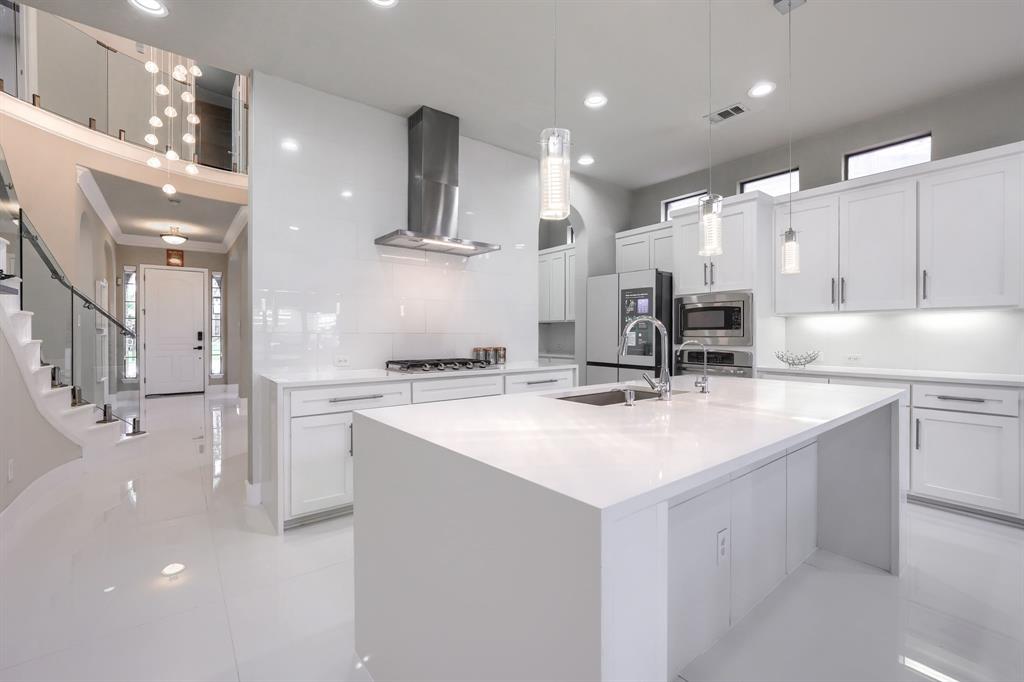 2246 Longview Road Irving, TX 75063 - Photo 9 of 40 Modern kitchen featuring a large central island with an undermount sink, white cabinetry, integrated stainless steel appliances, a tile backsplash, and recessed lighting