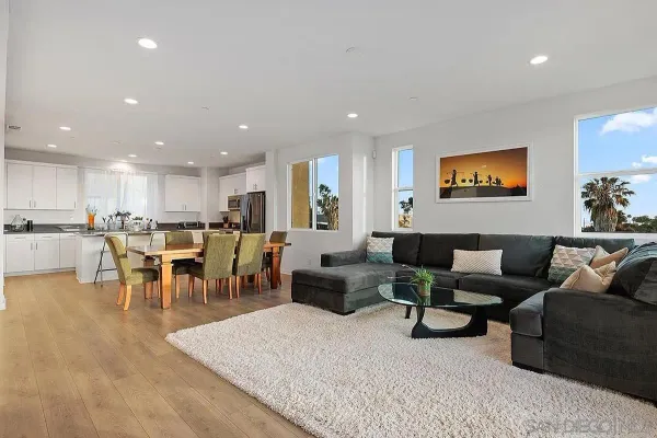 a living room with lots of furniture kitchen view and a large window