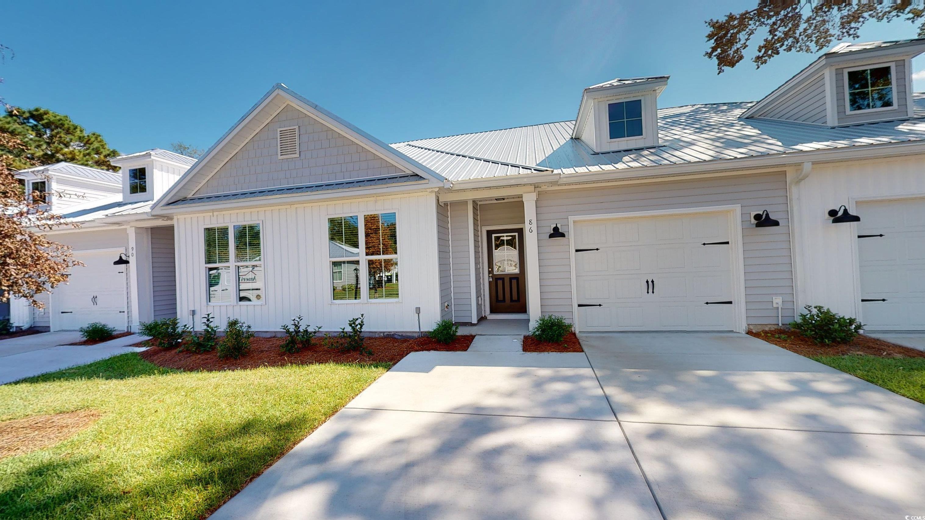 View of front of home featuring a metal roof, board and batten siding, driveway, and a front yard