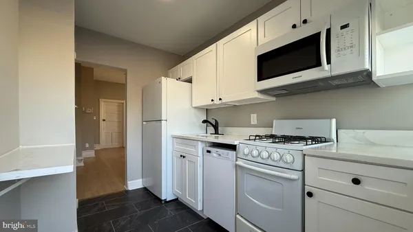 a kitchen with stainless steel appliances granite countertop white cabinets a sink a stove a refrigerator and microwave with wooden floor