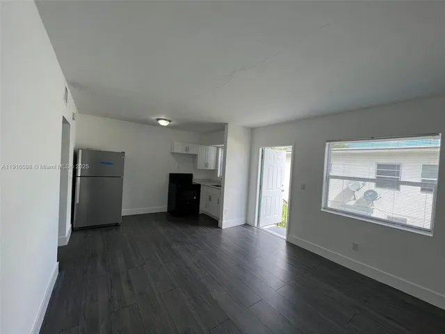 an empty room with wooden floor kitchen view and a window