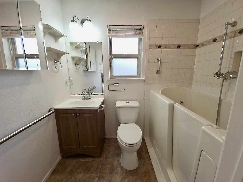 4901 Wing Road Austin, TX 78749 - Photo 16 of 28 Bathroom featuring a walk-in tub, white tiled walls with a decorative accent band, a single vanity with a white countertop, and a mirrored medicine cabinet