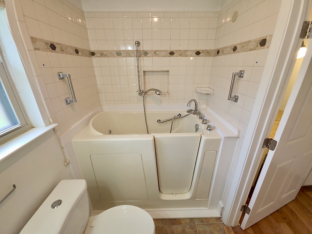 4901 Wing Road Austin, TX 78749 - Photo 17 of 28 Bathroom featuring a walk-in tub with chrome fixtures, tiled walls with decorative accents, a window with frosted glass, and grab bars