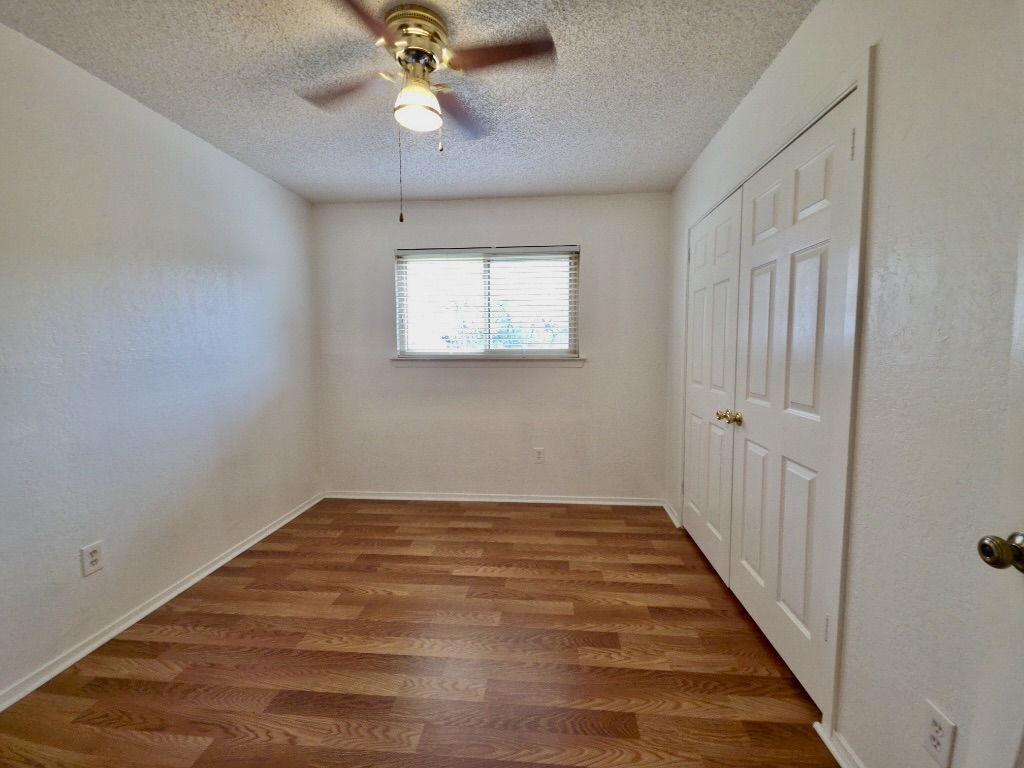 4901 Wing Road Austin, TX 78749 - Photo 18 of 28 Room featuring wood-finish flooring, a window with blinds, a ceiling fan with light fixture, and bifold closet doors