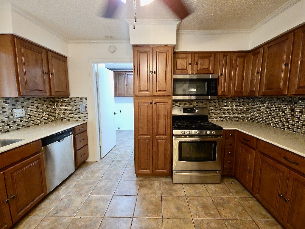 4901 Wing Road Austin, TX 78749 - Photo 7 of 28 Kitchen featuring wood-finish cabinetry, stainless steel appliances, tile flooring, mosaic tile backsplash, and light-toned countertops