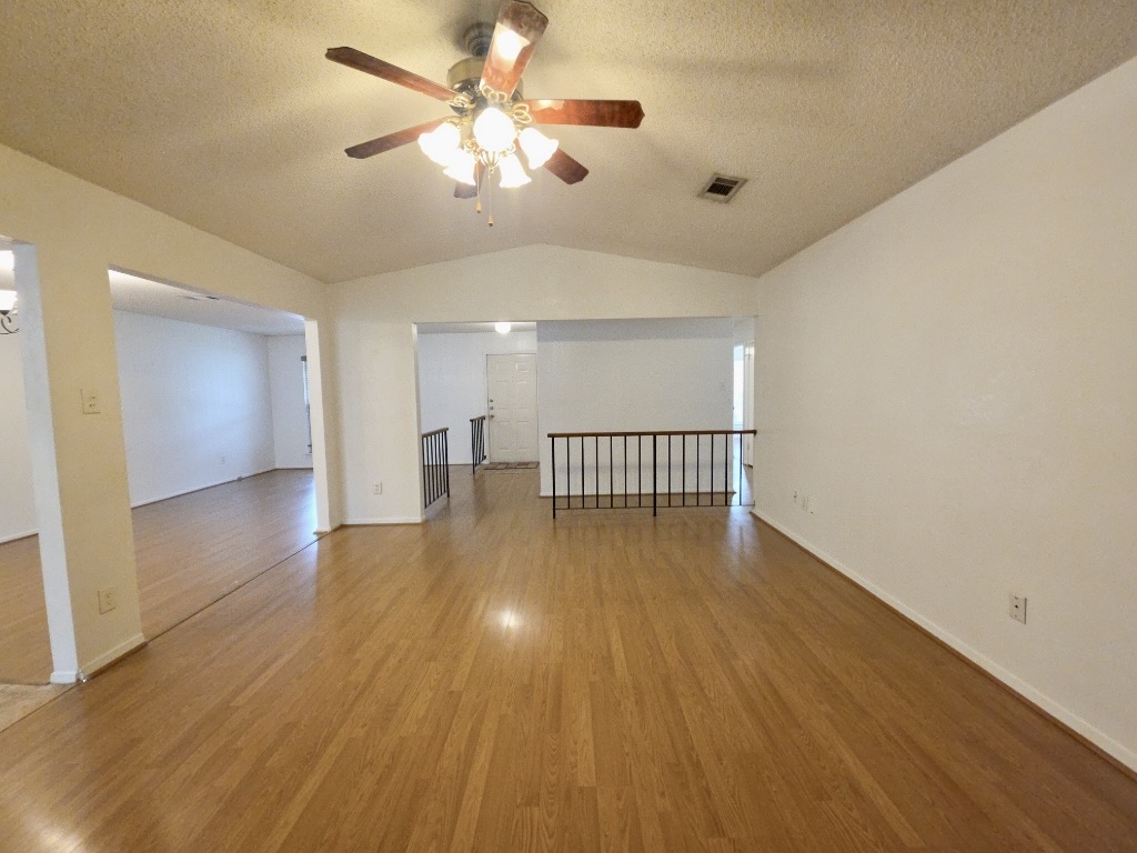 4901 Wing Road Austin, TX 78749 - Photo 28 of 28 Vaulted ceiling with a ceiling fan light fixture, wood-finish flooring, white painted walls, and an open floor plan